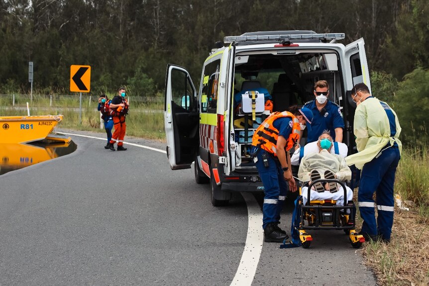 Several paramedics surrounding a man on a stretcher, near an ambulance.