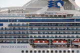 Close up view of a large ship called the Coral Princess. Red life boats are attached to its side. 