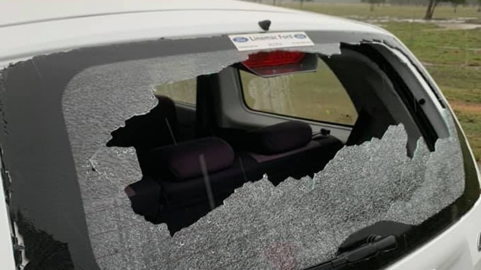 A small white car with its back window smashed in by hail.