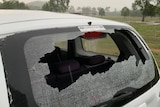 A small white car with its back window smashed in by hail.