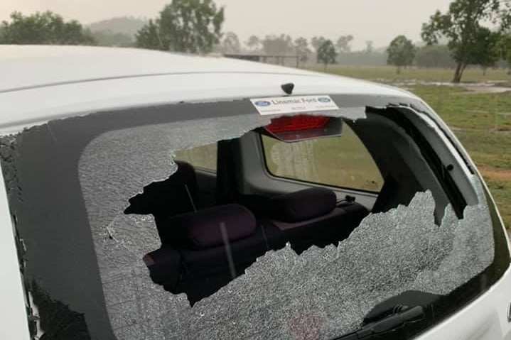 a small white car with it's back screen smashed in by hail