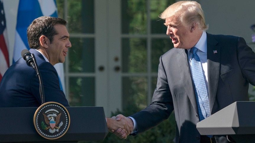 Donald Trump shaking hands with Alexis Tsipras from behind podiums at a press conference at the White House.