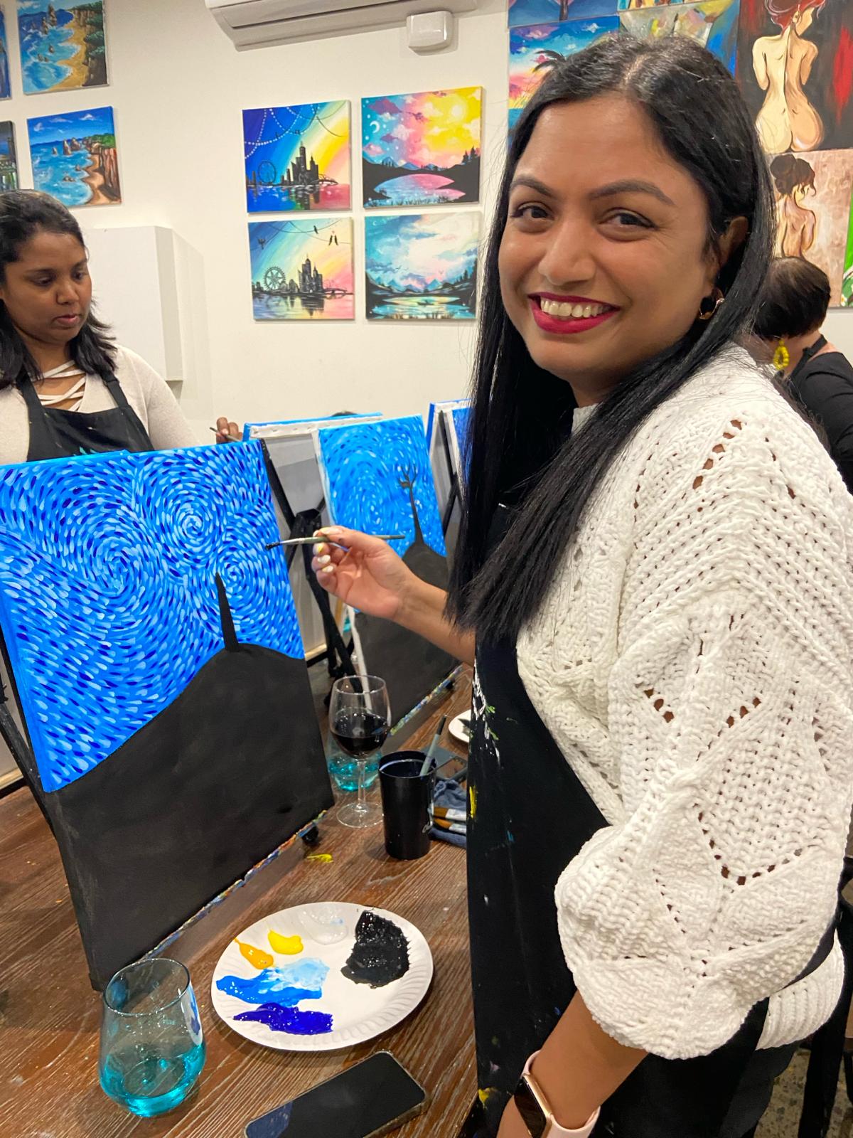 A woman smiling at the camera while painting.