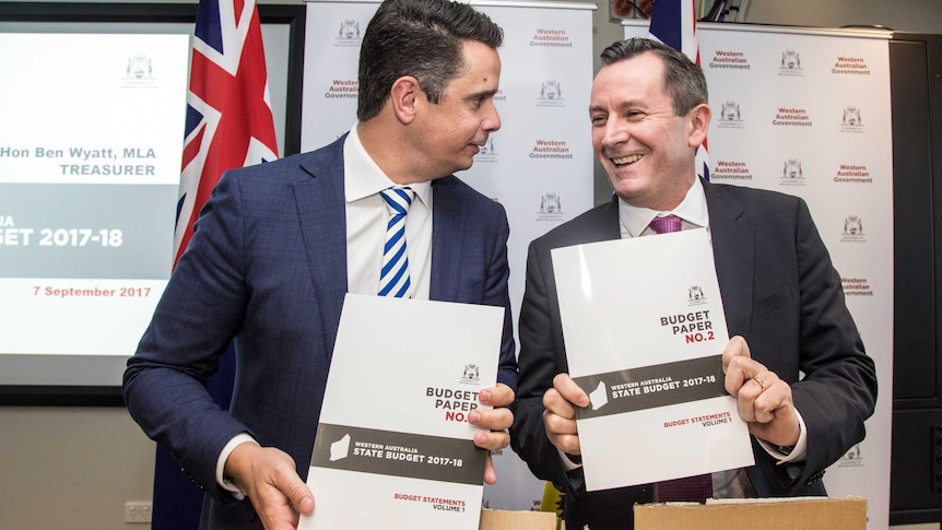 WA Premier Mark McGowan and WA Treasurer Ben Wyatt stand next to each other smiling and holding the 2017 State Budget.