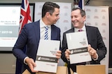WA Premier Mark McGowan and WA Treasurer Ben Wyatt stand next to each other smiling and holding the 2017 State Budget.