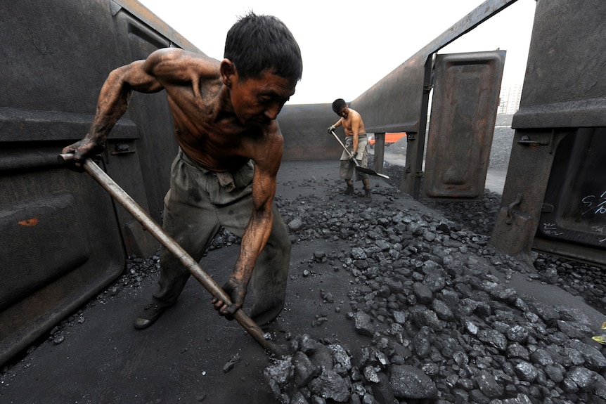 A shirtless man covered in soot shovelling coal out of the back of a truck