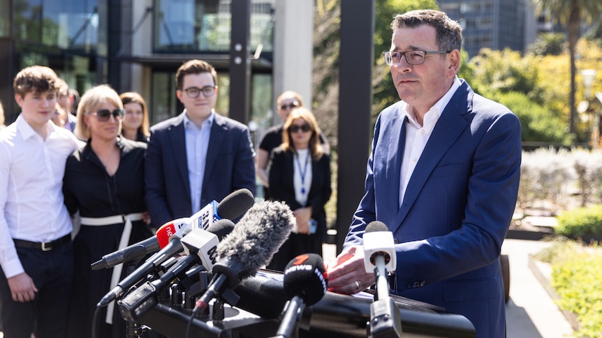 Daniel Andrews surrounded by media and microphones.