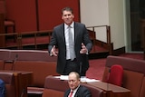 Wearing a black suit, Cory Bernadi stands and gestures while speaking in the Senate.