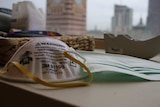 A P2/N95 mask and a surgical mask are placed on a desk in front of a window with a city skyline view.