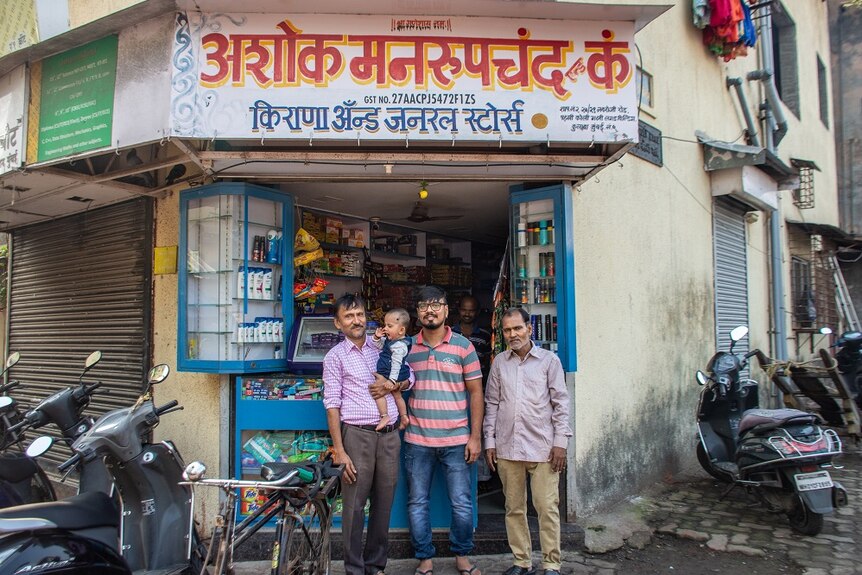 Three men and a baby standing outside a shop
