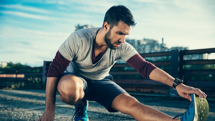 Young athletic man crouched down and stretching his calf