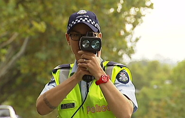 A police officer with a speed camera held up to his face.
