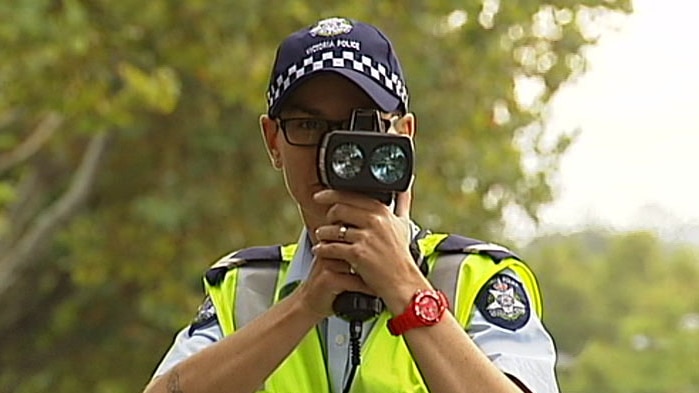 A police officer with a speed camera held up to his face.