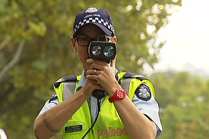 A police officer with a speed camera held up to his face.