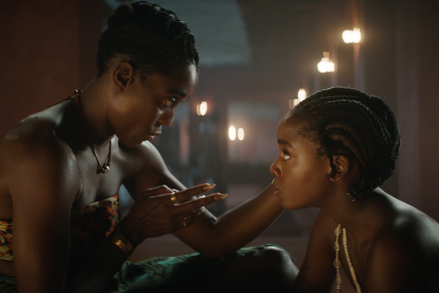 Two Black women with braided hair look into each other as the elder of the two seems to  giving advice in an intimate moment.