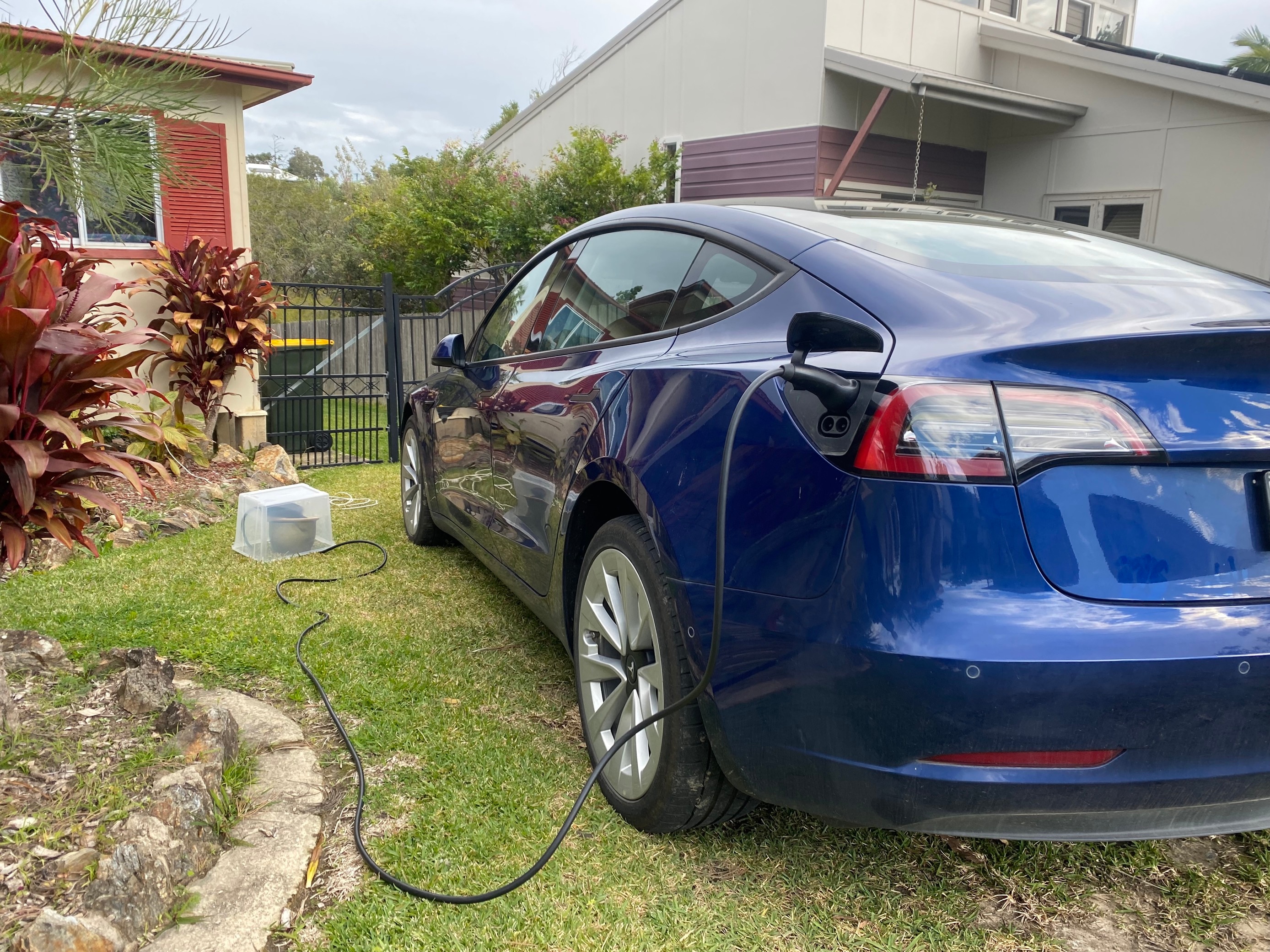 Un vehículo eléctrico cargándose frente a una casa suburbana 