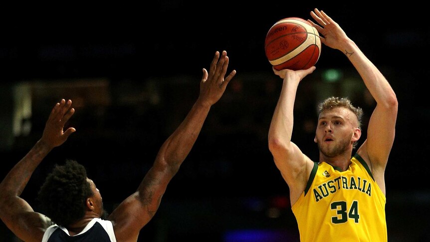 A male basketballer shoots for a basket with his right hand as an opponent attempts to block.