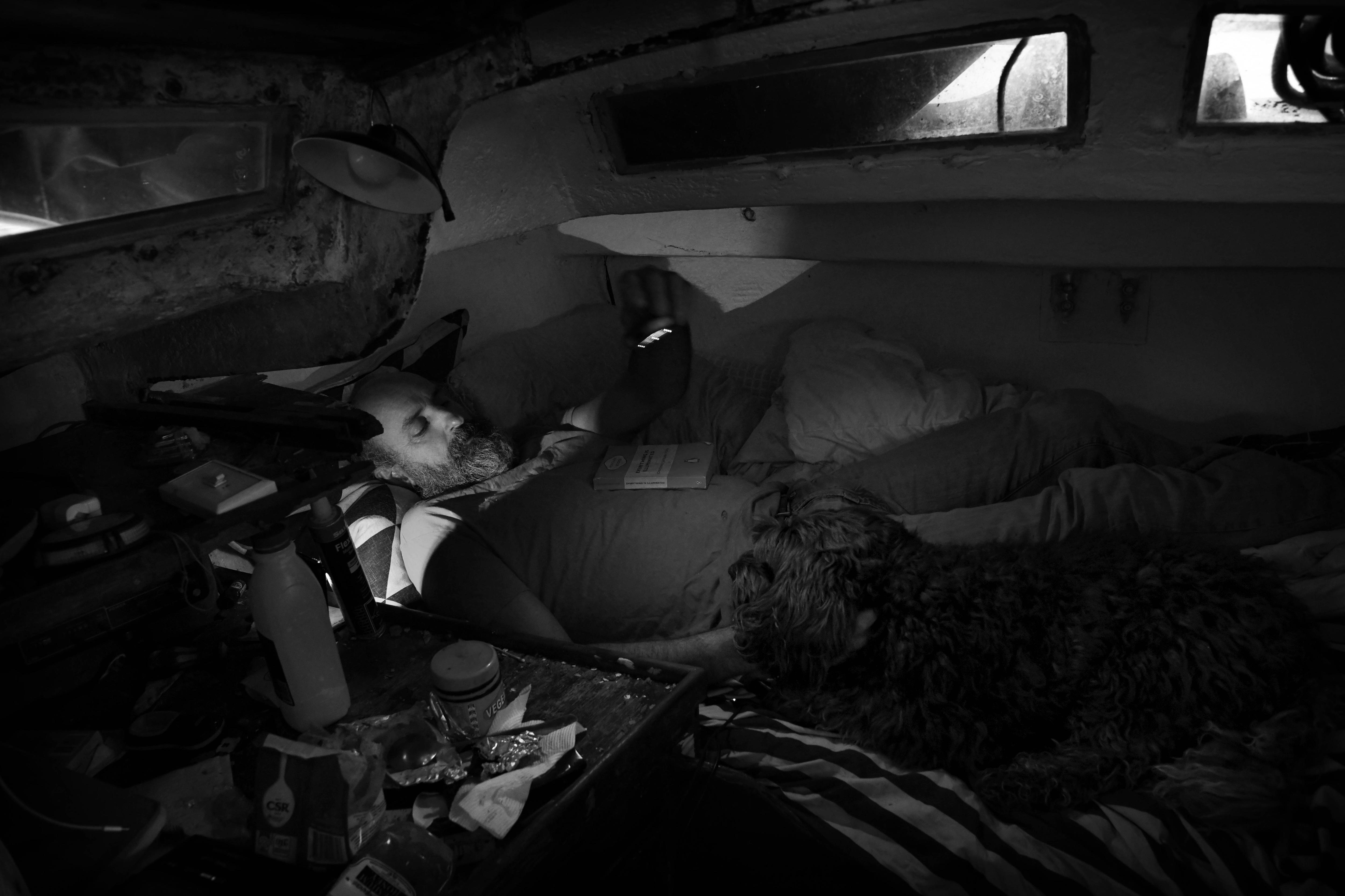 A man lies down in the bed petting his dog 