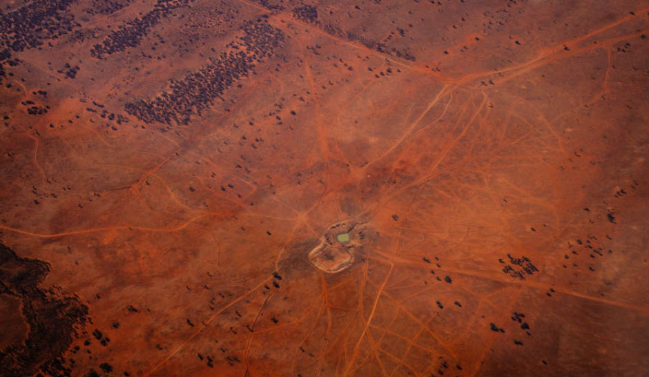 Aerial of waterhole surrounded by red dust