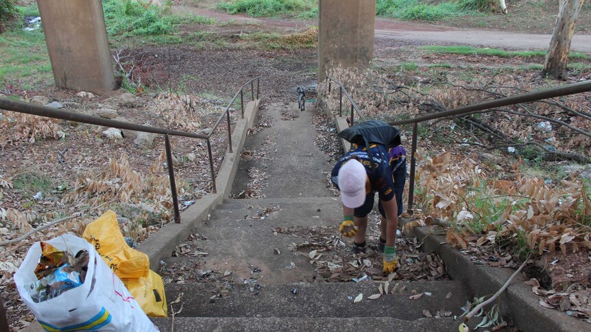 A woman on long stairs collecting rubbish in the Katherine bush.