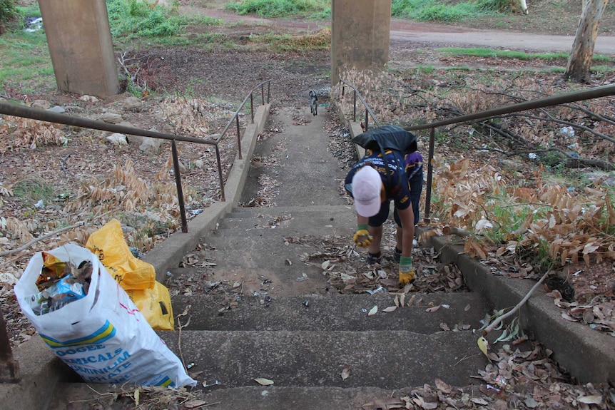 A woman on long stairs collecting rubbish in the Katherine bush.