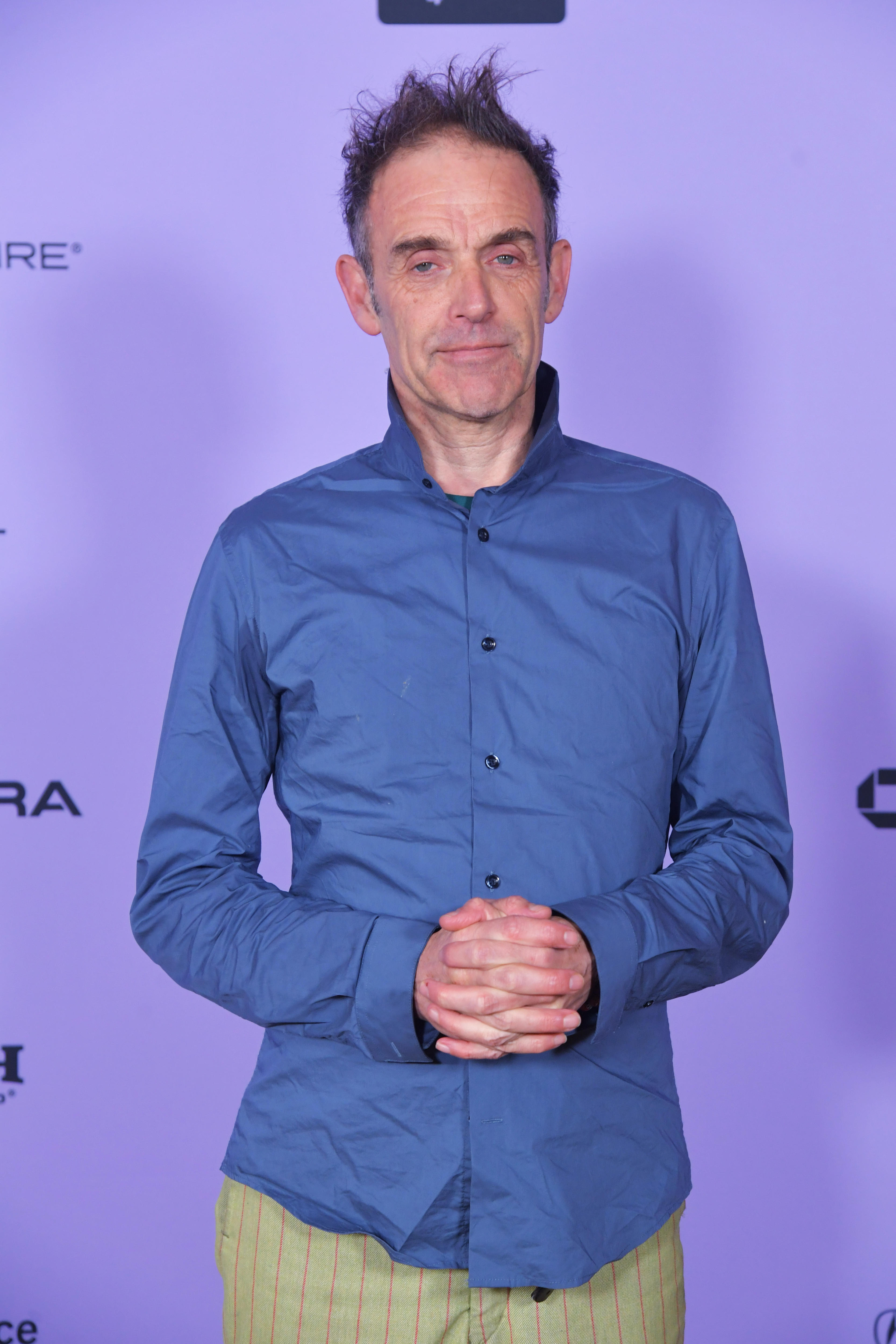 Man with bright blue shirt and ruffled dark hair smiles at the camera