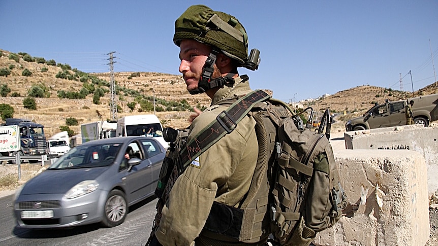 An Israeli soldier watches cars drive through a pop-up checkpoint near Beni Neiem village.