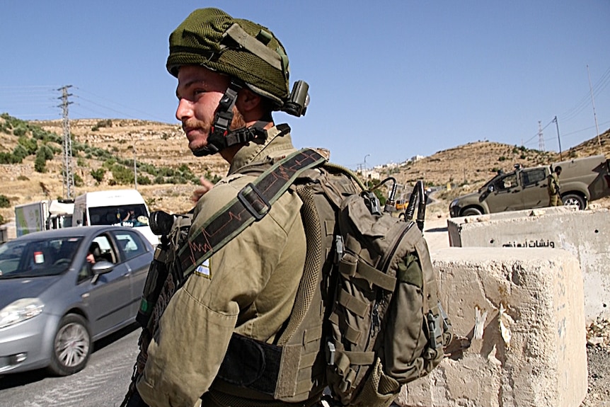 An Israeli soldier watches cars drive through a pop-up checkpoint near Beni Neiem village.