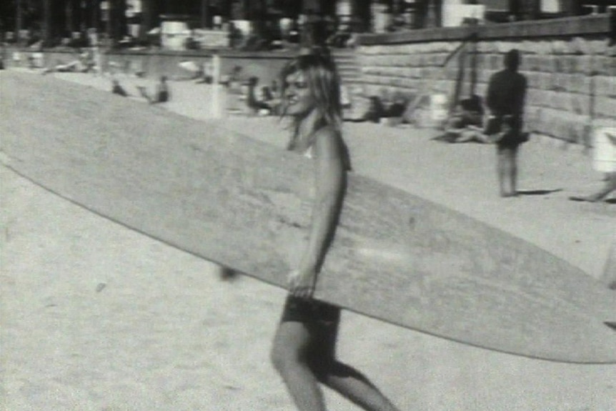 A black and white image of a woman holding a surfboard.
