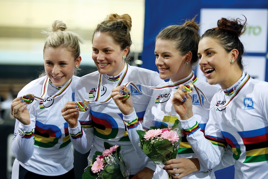 Four women smile holding up medals and wearing matching rainbow cycling jerseys.