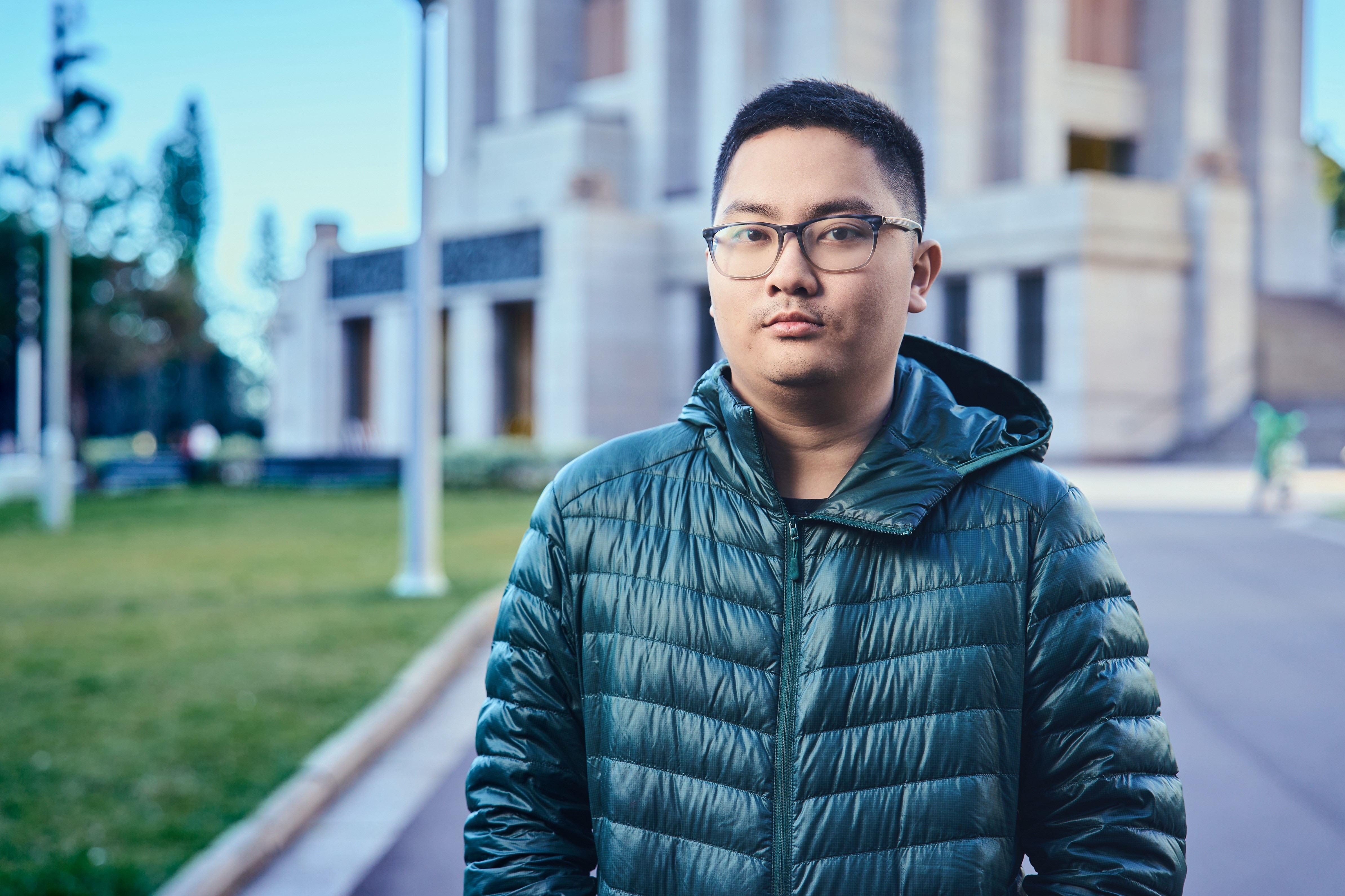 student Brandon Lim wears glasses and a puffer jacket as he stands outdoors looking at the camera