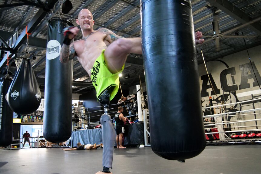 A man with a prosthetic leg kicks a boxing bag with his other leg.