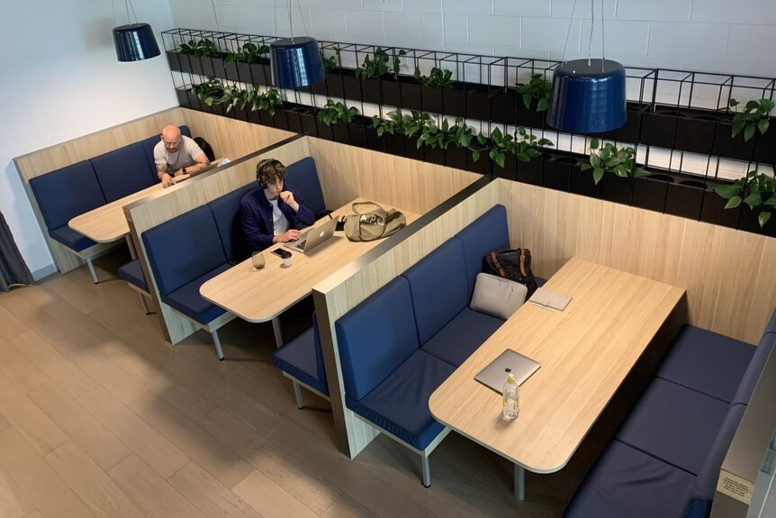 A row of three tables in a cafe with two people working.