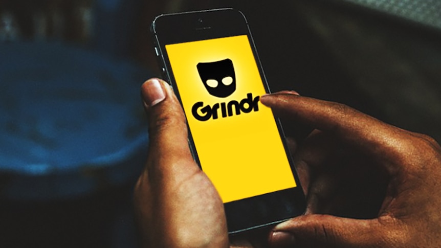 Unidentified male hands holding smartphone with dating app Grindr logo on screen.