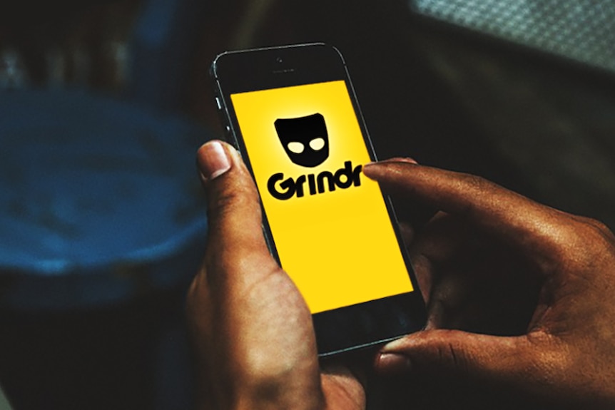 Unidentified male hands holding smartphone with dating app Grindr logo on screen.