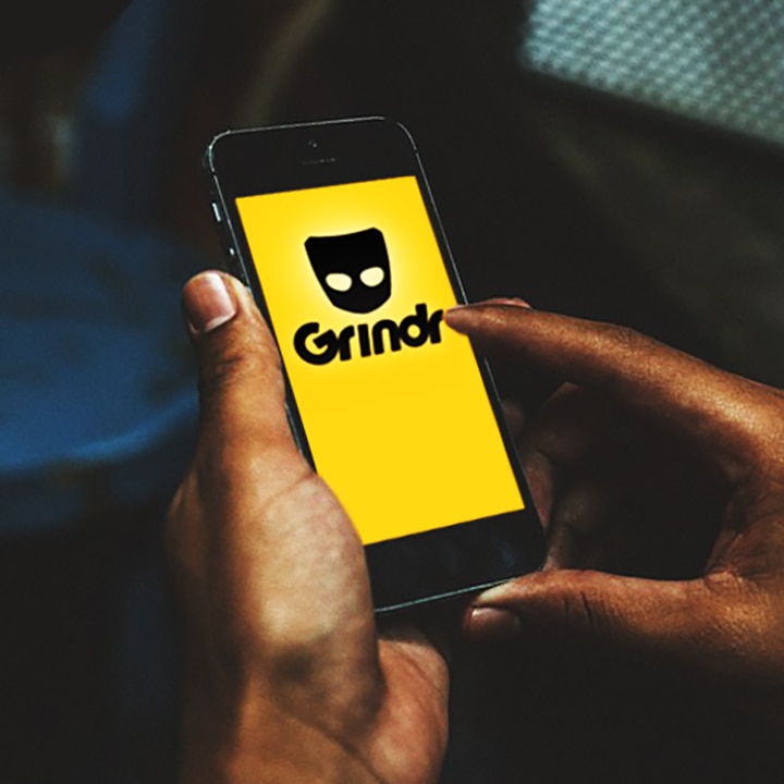 Unidentified male hands holding smartphone with dating app Grindr logo on screen.