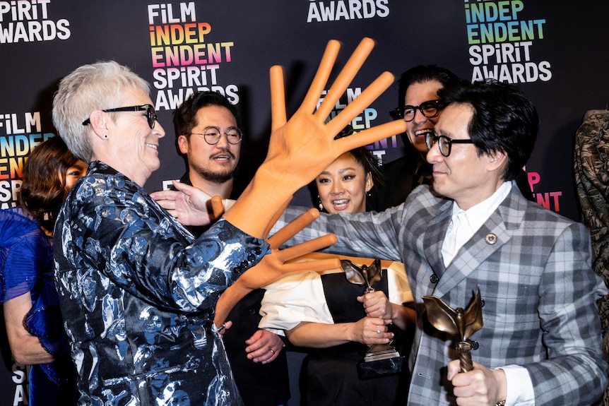 A woman wearing oversized rubber hands moves to hug a man.