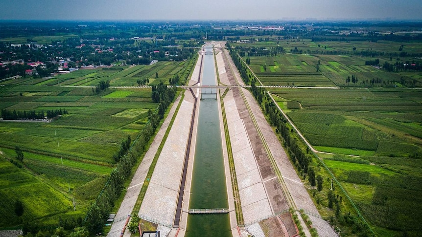 Aerial view of a water transfer canal stretching from a rural area towards a city.