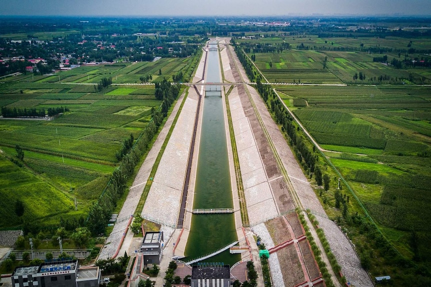 Aerial view of a water transfer canal stretching from a rural area towards a city.