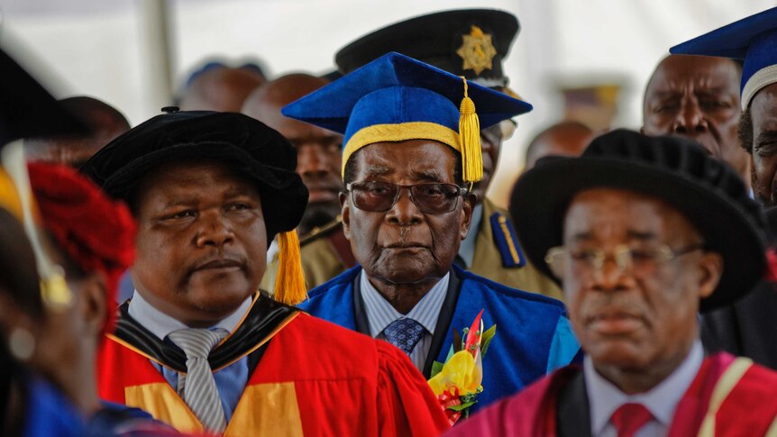 Robert Mugabe wears a blue and yellow graduation gown and walks in a crowd