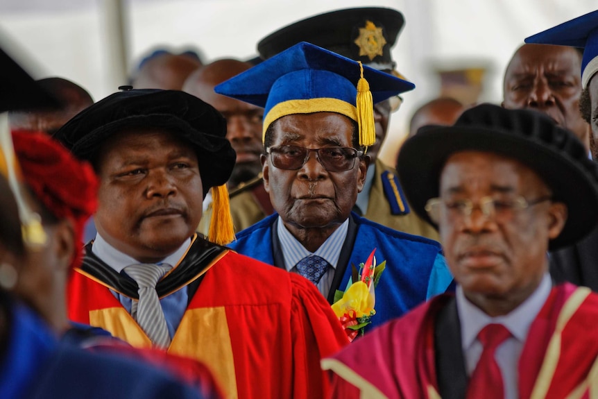 Robert Mugabe wears a blue and yellow graduation gown and walks in a crowd