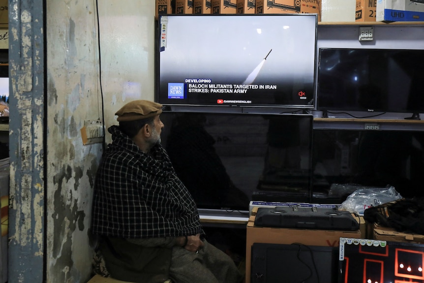 A man watches a news channel on television inside a shop.