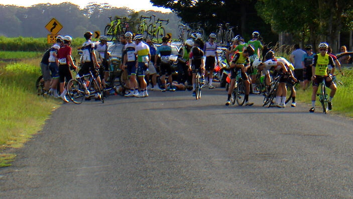 A group of cyclists stopped on a road with cars behind.