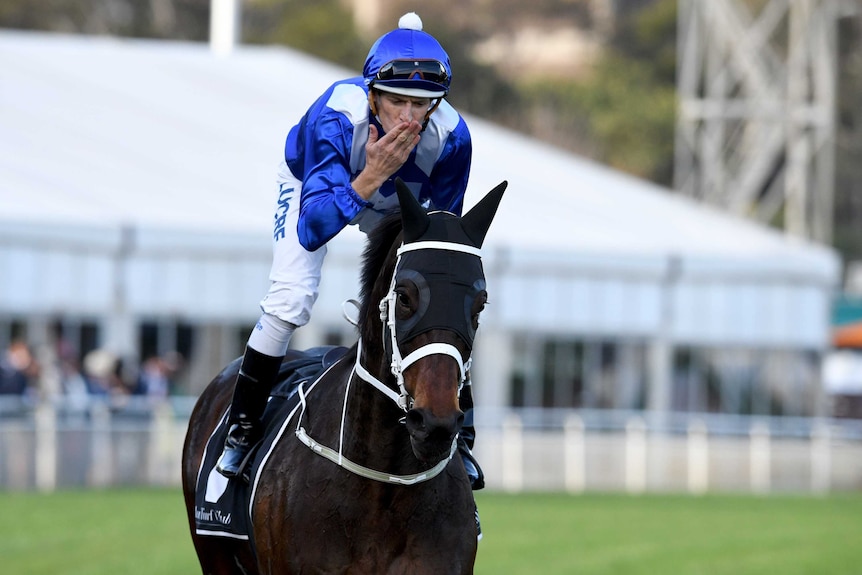 Hugh Bowman kisses his hand as he rides Winx back to the mounting yard.