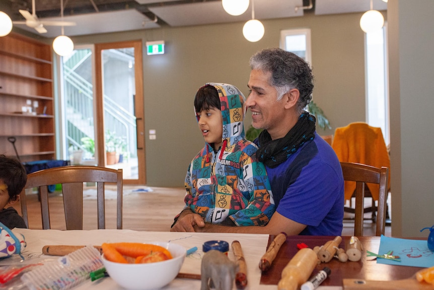 A man and young boy sit at a dining table with toys on it.