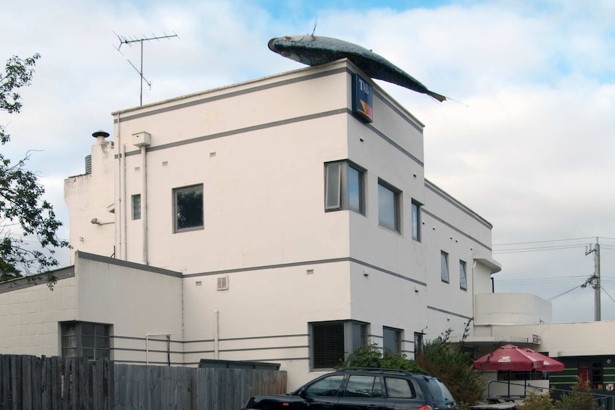 A two story white hotel with a dead fish sculpture on the top corner of its roof in Fish Creek Victoria.