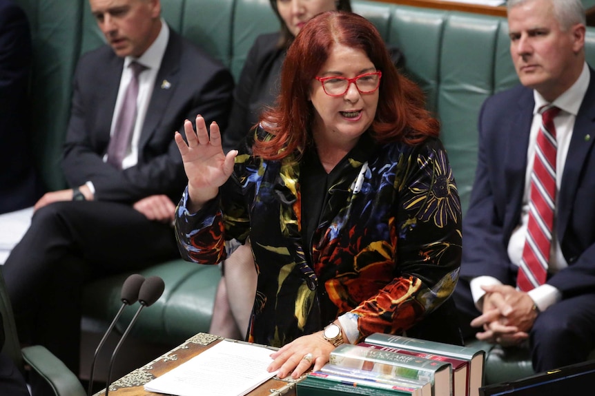 A red-haired woman stands at a podium with arm raised.