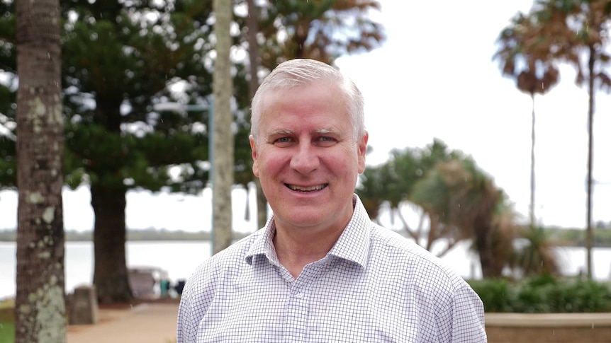 Man aged in his mid-fifties smiling at the camera. He has short light grey hair and is wearing a white shirt with blue checks.