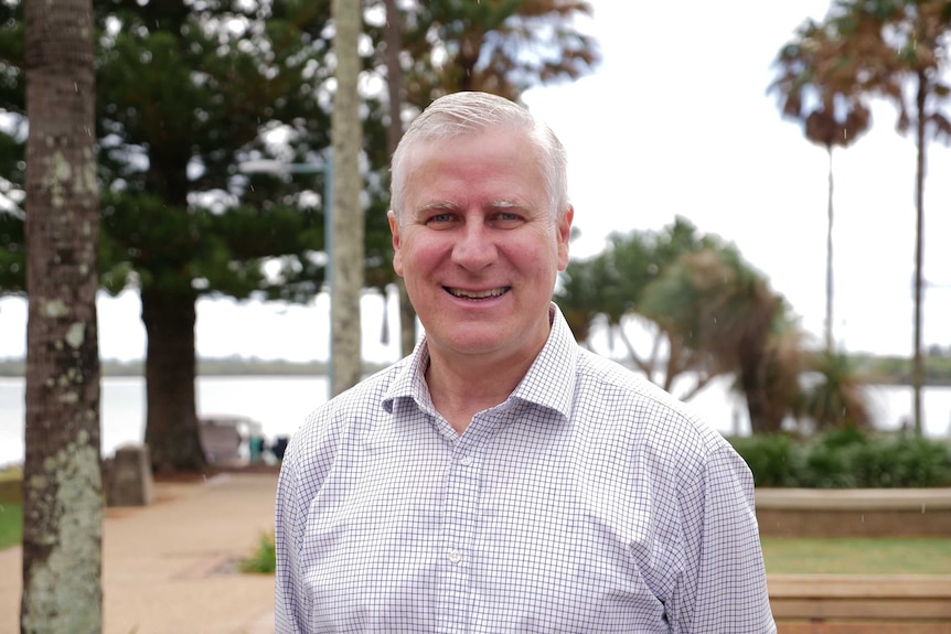 Man aged in his mid-fifties smiling at the camera. He has short light grey hair and is wearing a white shirt with blue checks.