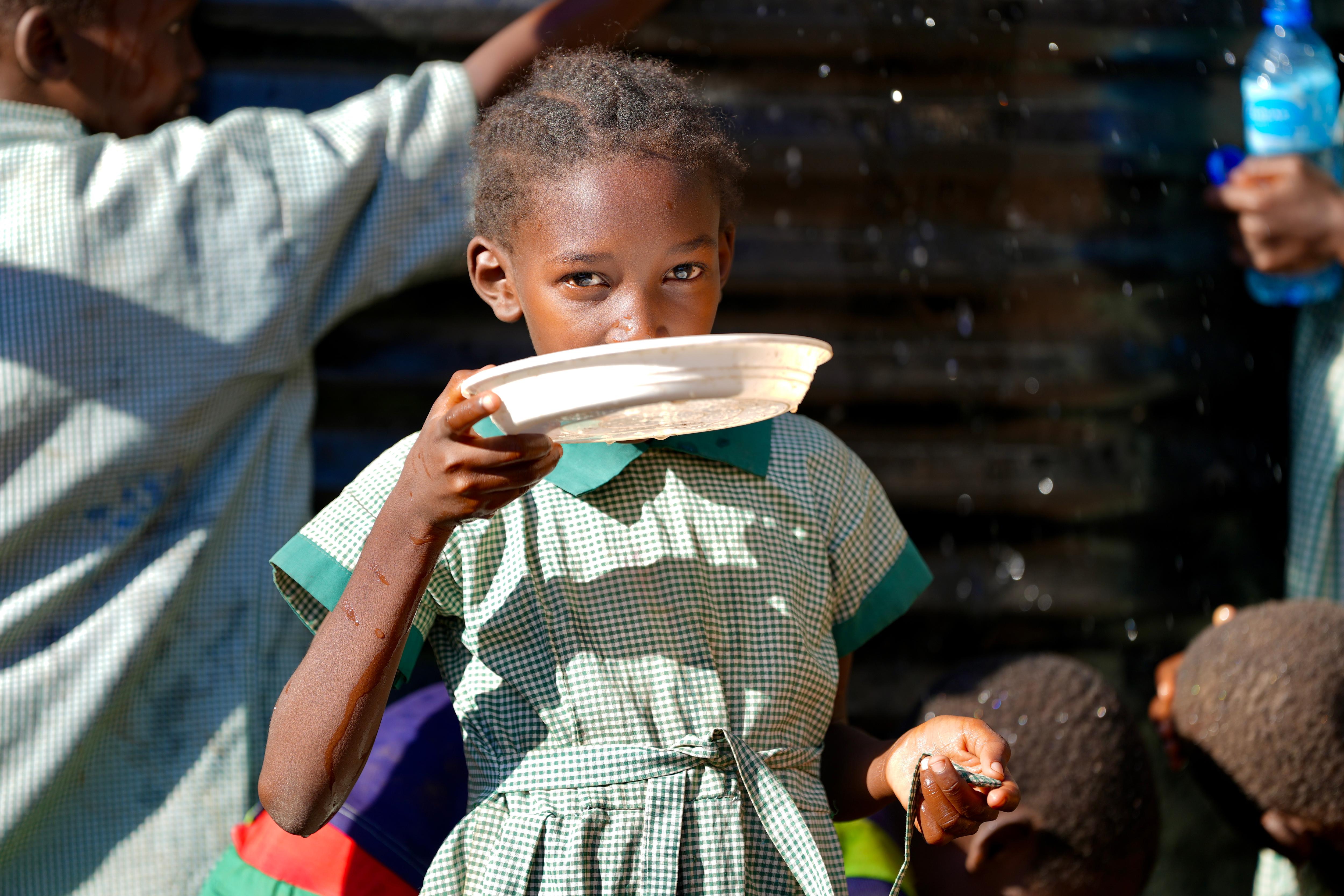 A young kenyan girl drinking water from a plastic bowl.
